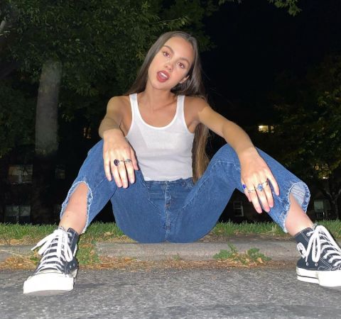 Olivia Rodrigo in a white top and blue jeans poses a picture.
